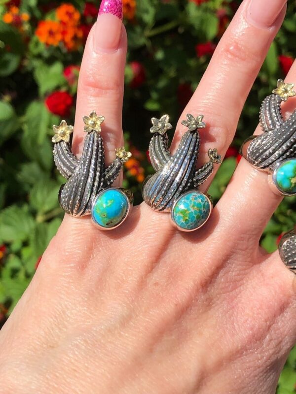 A hand holding up four rings with cactus designs on them.