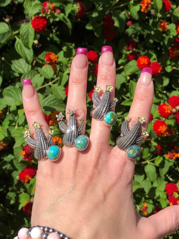 A hand with multiple rings on it and flowers in the background