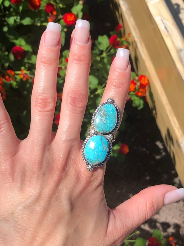 A woman 's hand is holding up a turquoise ring.