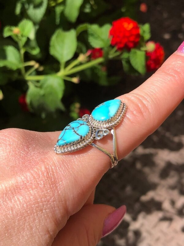 A woman is holding her ring with two turquoise stones.