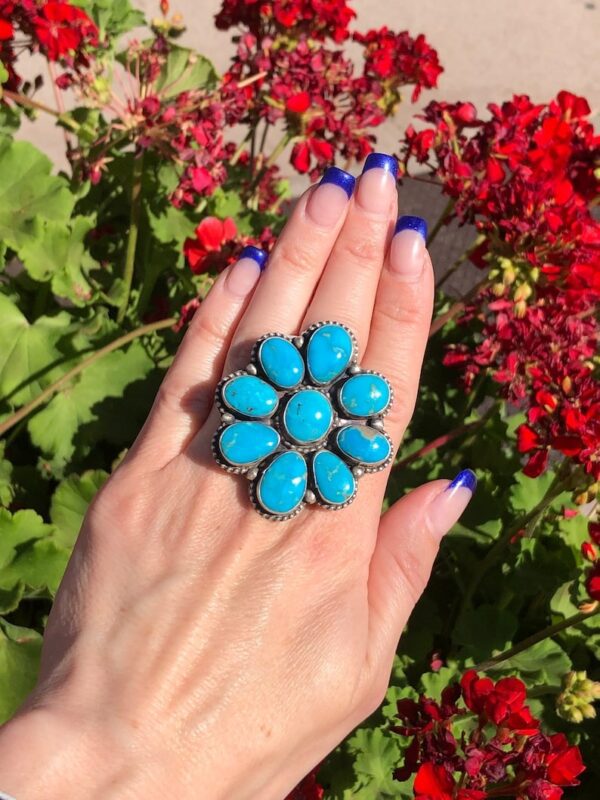 A woman is holding her hand up to the top of a flower shaped ring.