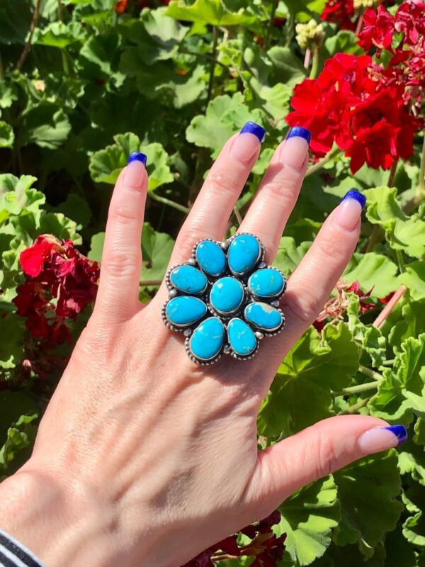 A woman 's hand is holding up a turquoise ring.