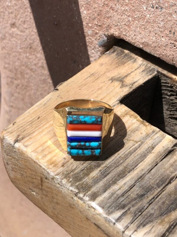 A gold ring with multi colored stones on top of a wooden box.