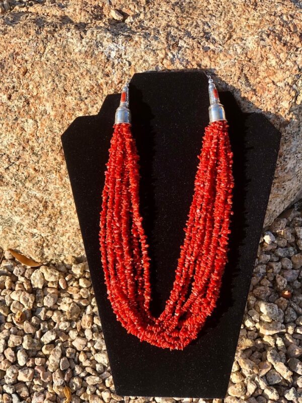 A necklace of red beads is displayed on a black stand.