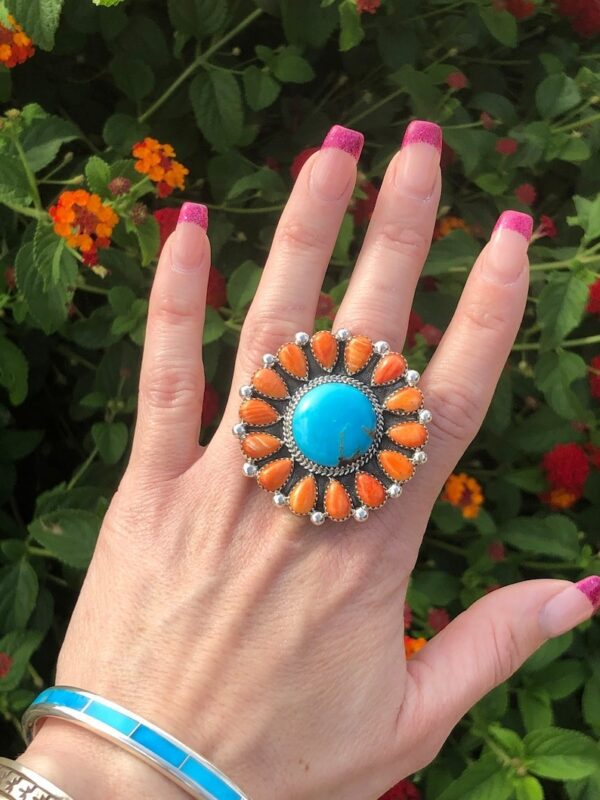 A woman 's hand wearing a ring with orange and blue stones.