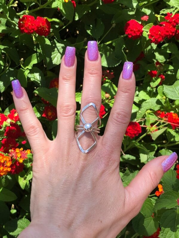 A woman 's hand with purple nails and a silver ring on her finger.