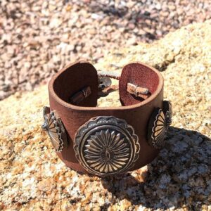 A brown leather bracelet with silver conchos on it.