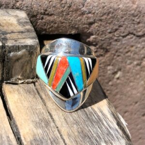 A silver ring with multi colored stones on top of a wooden surface.
