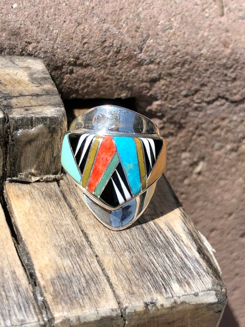 A silver ring with multi colored stones on top of a wooden surface.