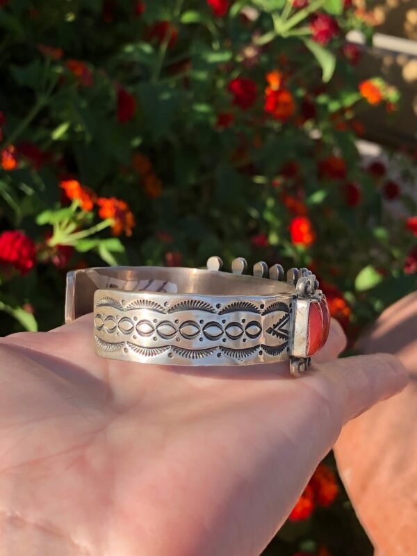 A person holding onto a silver bracelet with red stones