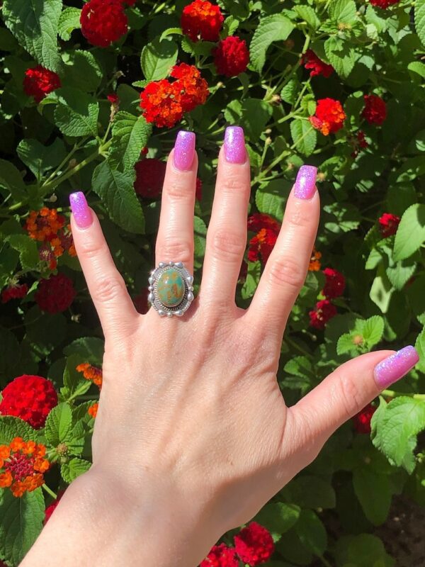 A woman 's hand with purple nails and a green ring on her finger.