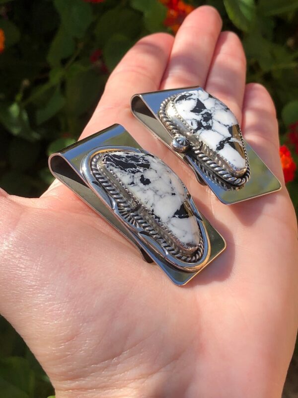 A person holding two silver money clips with white and black stones.