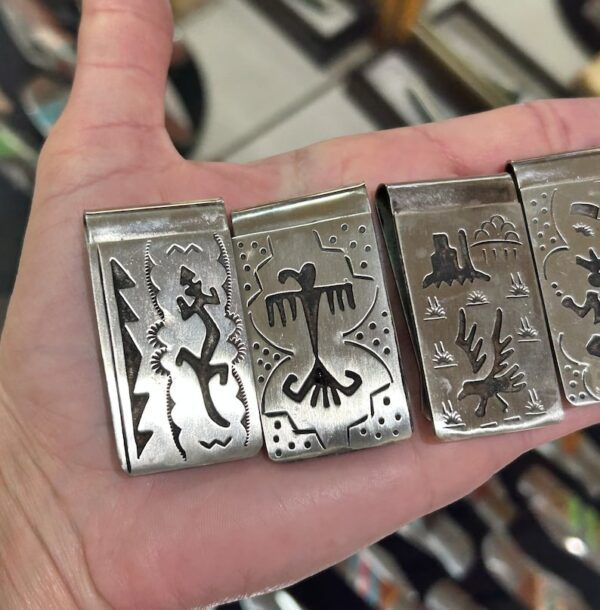 A hand holding four different metal money clips.
