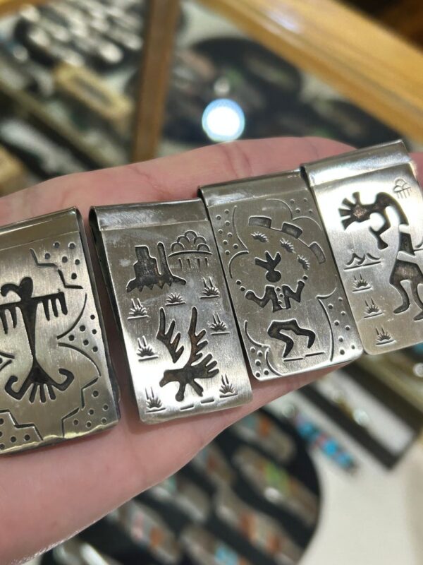 A hand holding four silver money clips with designs on them.
