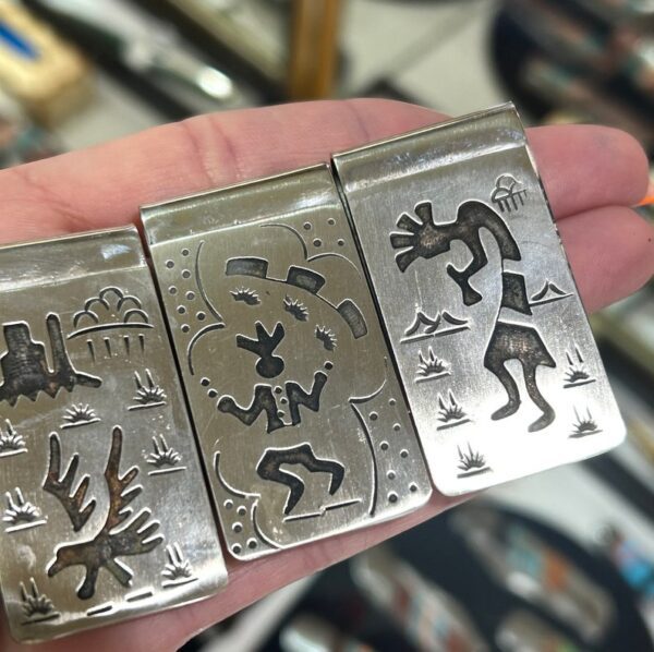 A hand holding three silver money clips.