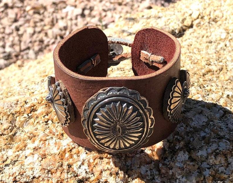 A brown leather bracelet with silver conchos.