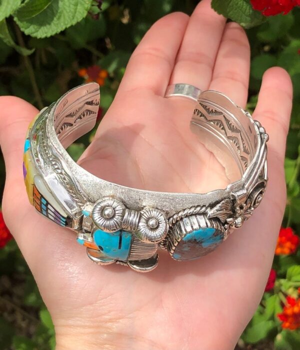 A hand holding a silver bracelet with turquoise stones.