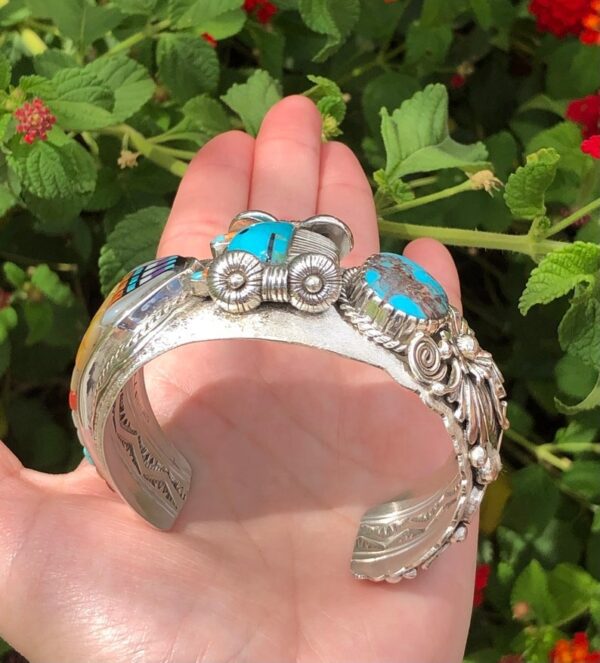 A hand holding a silver bracelet with cars on it.
