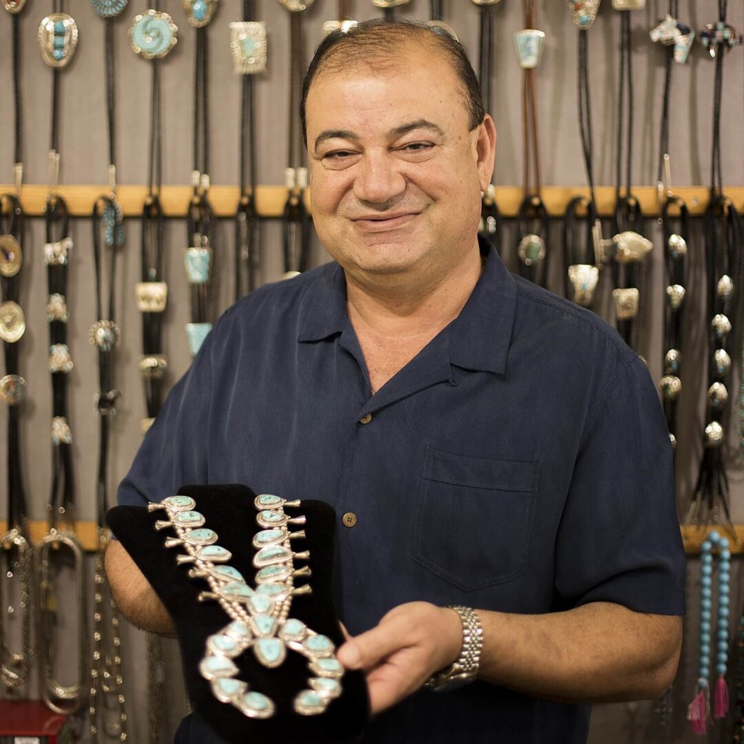 A man holding a necklace in front of many necklaces.