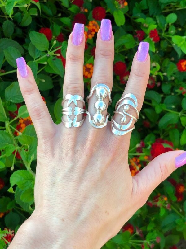 A woman 's hand with purple nails and three rings on her fingers.