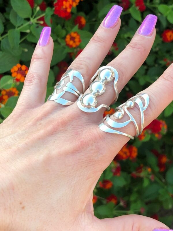 A hand with three rings on it and purple nails