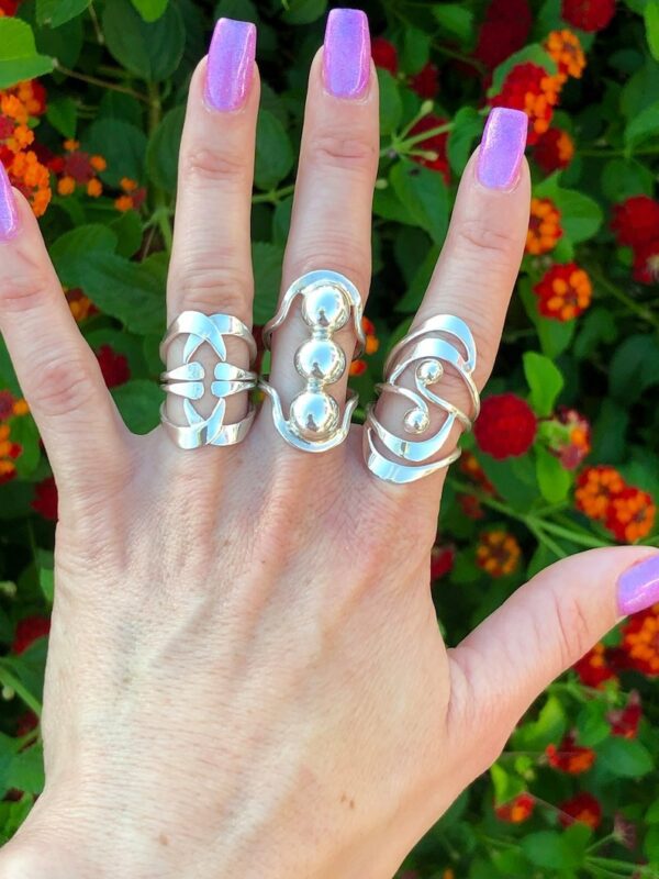 A hand with three rings on it and purple nails