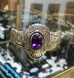 A purple stone is on the side of a silver bracelet.