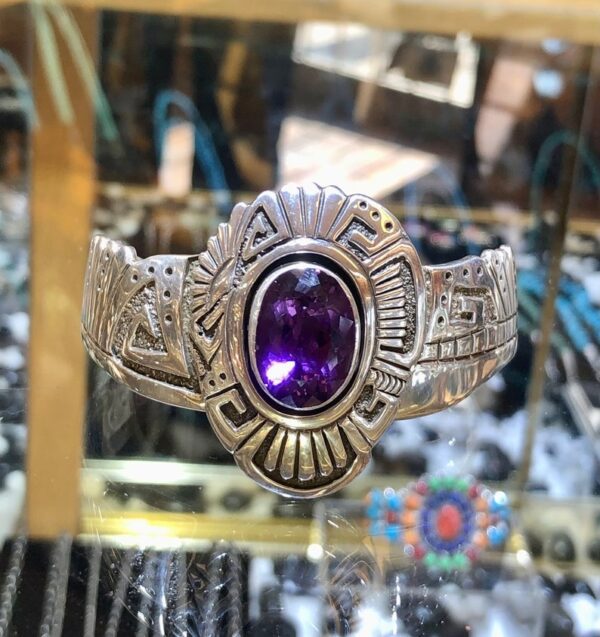 A purple stone is on the side of a silver bracelet.