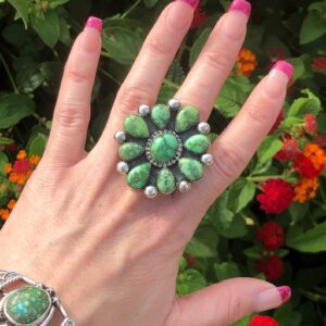 A woman 's hand is holding up a ring of green stones.