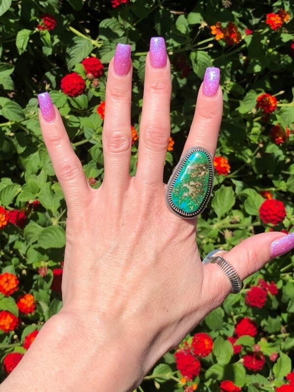 A woman 's hand with purple nails and green nail polish.