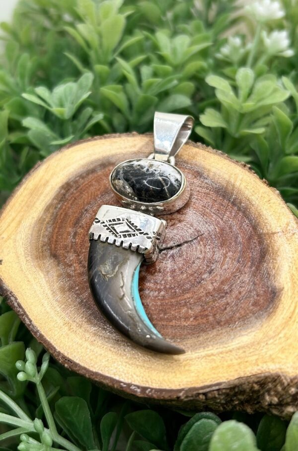 A silver and turquoise pendant on top of a wooden log.