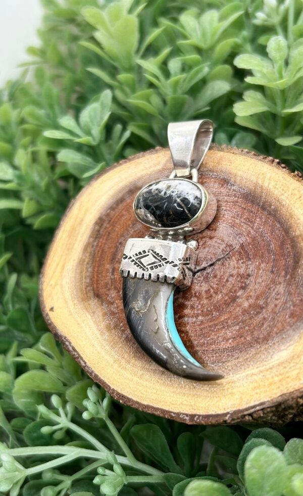 A silver pendant with a black stone and turquoise inlay.