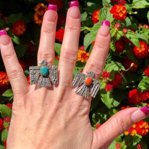 A woman's hand with a pair of Hammered Antique Oxidized Sterling Silver Turquoise + Coral Thunderbird Rings Unisex Henry Yazzie and a turquoise ring.