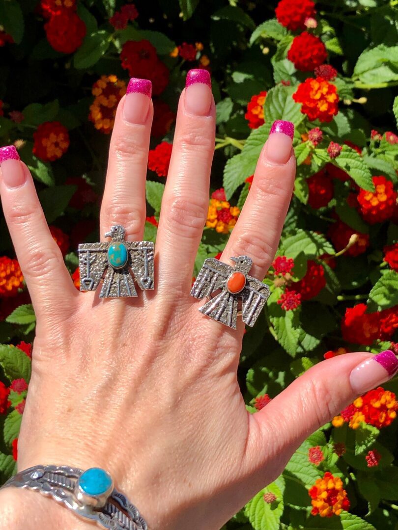 A woman's hand with a pair of Hammered Antique Oxidized Sterling Silver Turquoise + Coral Thunderbird Rings Unisex Henry Yazzie and a turquoise ring.