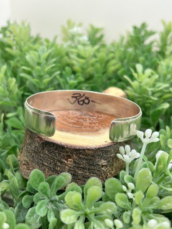 An Augustine Mowa Jr. Hopi Symbols Sterling Silver Cuff Bracelet sitting on top of a piece of wood.