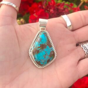 A hand holding a turquoise pendant.