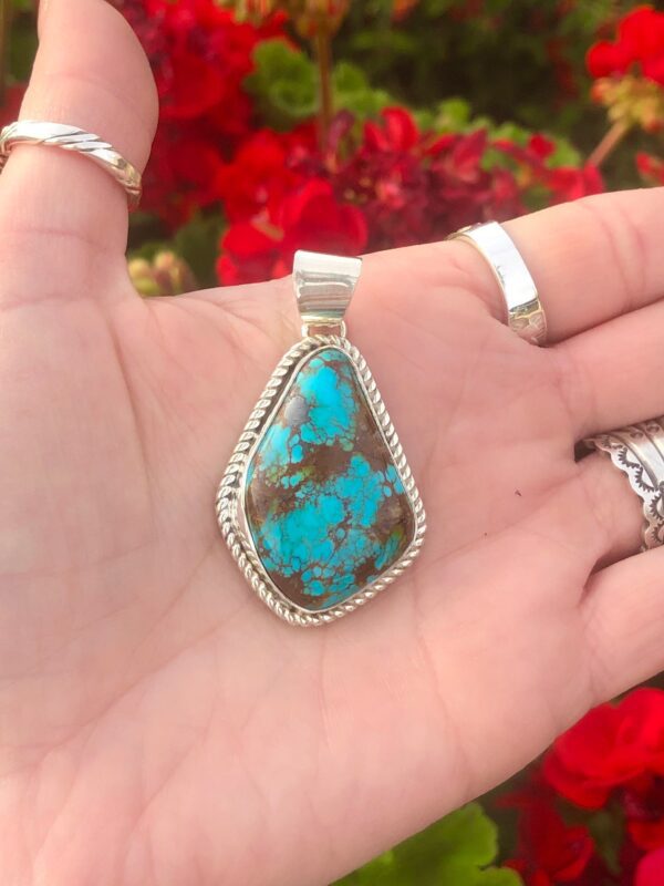 A hand holding a turquoise pendant.