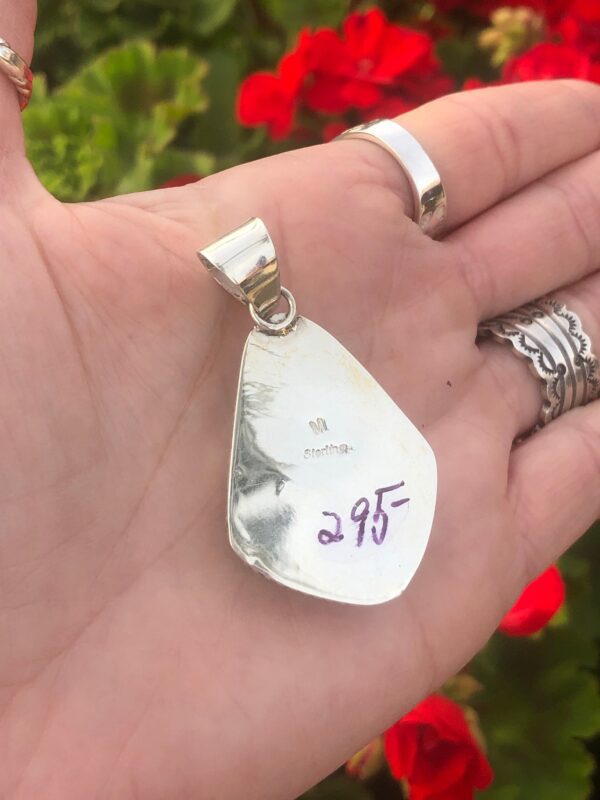 A silver pendant with a purple stone in the palm of a hand.