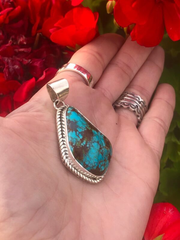 A hand holding a silver pendant with a blue turquoise stone.