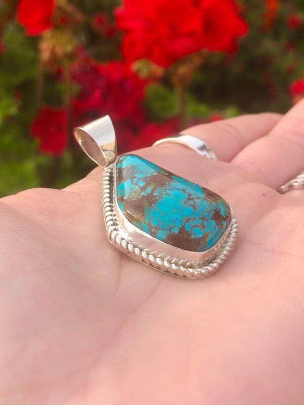 A hand holding a turquoise pendant.