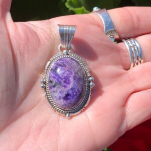 A hand holding a silver pendant with a purple stone.