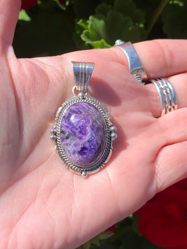 A hand holding a silver pendant with a purple stone.