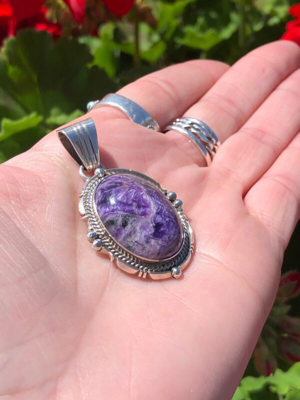 A hand holding a silver pendant with a purple stone.