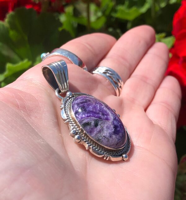 A hand holding a silver pendant with a purple stone.