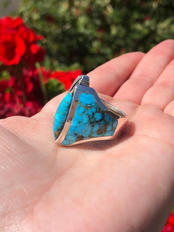 A hand holding a silver ring with a large turquoise stone.