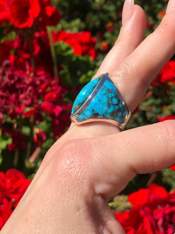 A hand wearing a silver ring with a blue turquoise stone.