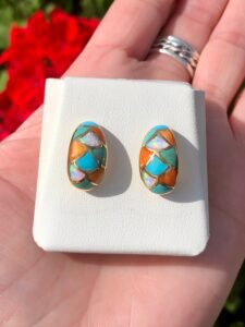 A person is holding a pair of turquoise and orange stud earrings.
