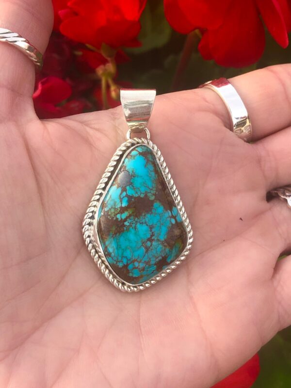 A silver pendant with a large turquoise stone.