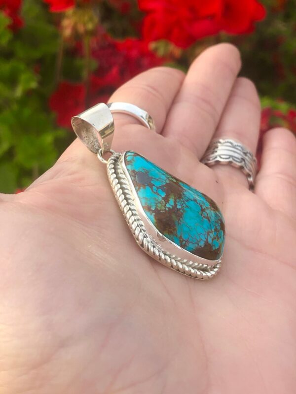 A hand holding a large turquoise pendant.