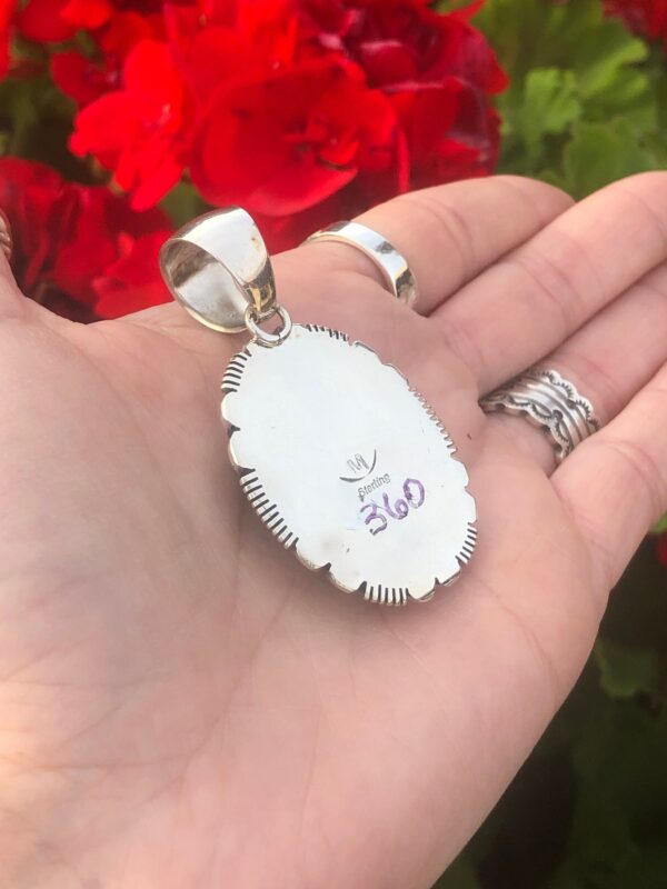 A silver pendant with red flowers in the background.